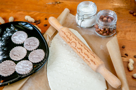 Rolling pin with a mustache pattern on a wooden decorated table covered with baked flour. Rolled dough with a pattern and cookie of various shapes. Biscuit cooking background, top view