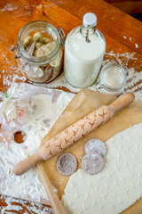 Fototapeta premium Rolling pin with a pattern on a wooden decorated table covered with baked flour. Rolled dough with a pattern and cookie of various shapes. Biscuit cooking background, top view
