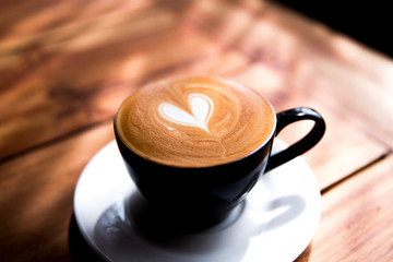 Cappuccino cup with heart latte art on wooden table background.