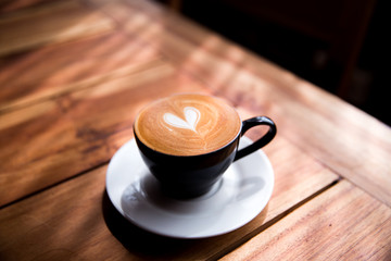 Cappuccino cup with heart latte art on wooden table background.