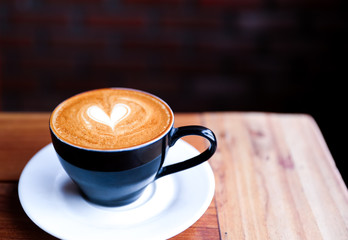 Cappuccino cup with heart latte art on wooden table background.