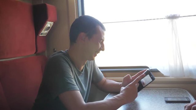 man traveler Relaxing On Train Listening To Music and smiling through the pictures via social media. slow lifestyle motion video. uploading photo using cell phone while riding home by train wagon