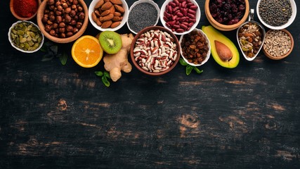 Various superfoods. Dried fruits, nuts, beans, fruits and vegetables. On a black wooden background. Top view. Free copy space.