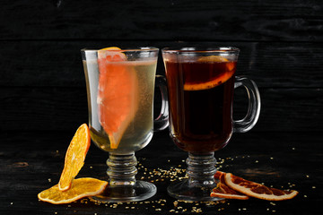 Hot wine with citrus fruit. Winter and autumn traditional cocktails. On a black wooden background....