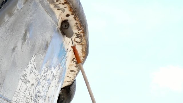 Worker paints metal of old rusty ship propeller at shipyard in port.