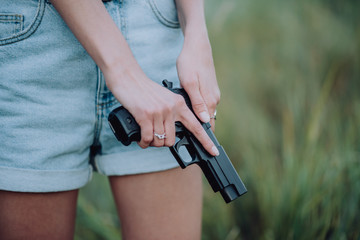 girl in denim shorts and with a gun in his hand posing in the field. Close up