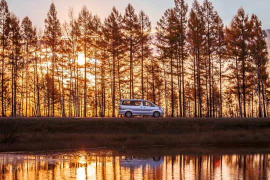 Silver minivan on foreat road at sunset