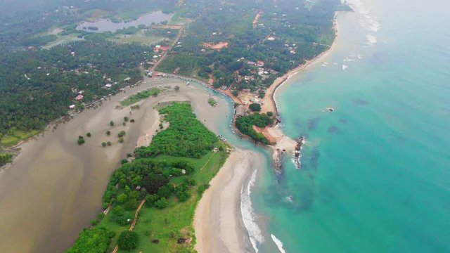 Aerial, tilt, drone shot of waves hitting a paradise coast, revealing Trincomalee town, on a cloudy day, in Gokanna, in the Eastern Province of Sri Lanka