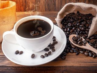 Hot coffee cup and coffee beans roating on the wood table