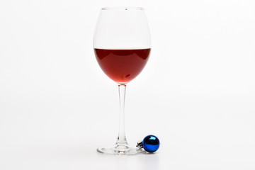 Glass with wine and christmas decoration. Winter celebration with alcohol drink. New year party concept. Wineglass with red liquid or wine and christmas ball ornament isolated on white background