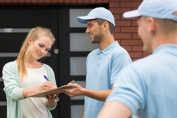 Smiling woman signing receipt from professional courier wearing blue uniform