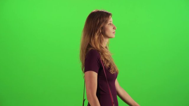 Young woman walking in a medium sideways shot over a green screen, answering a phone call happily, talking and hanging, two takes.
