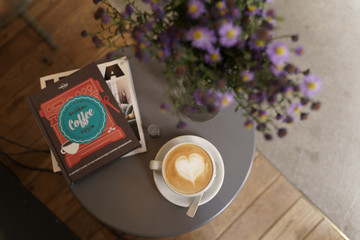 A table with a cup of coffee, books and purple flowers