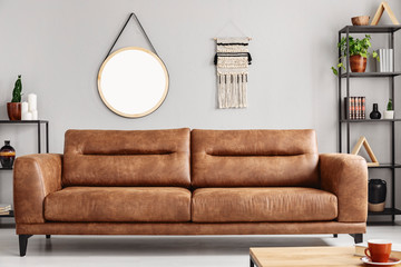 Mockup of round mirror on grey wall in living room interior with brown leather settee. Real photo