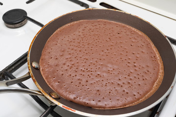 Dark chocolate pancake is fried in a pan