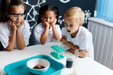 Group of multiracial diverse kids in scientist white clothes doing science experiments with reagents in the laboratory, being surprised and astonished with the results. Science and education in lab
