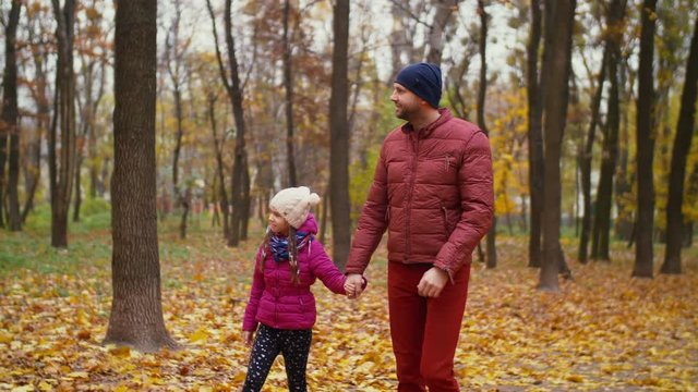 Carefree handsome father and adorable little girl enjoying beautiful autumn nature while taking a walk through public park in indian summer. Parent with child resting and bonding outdoors in autumn.