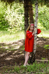 Blond young girl posing in a red dress near birch trees