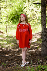Blond young girl posing in a red dress near birch trees