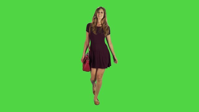 A young woman walking towards camera, laughing and looking into the lens in a full body shot over a green screen.