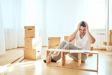 Concentrated young man reading instructions to assemble furniture at home