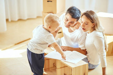family with little boy reading instruction and assemble furniture together at living room of new apartment pile of moving boxes on background