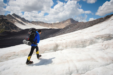 A mountaineer with a backpack walks in crampons walking along a dusty glacier with sidewalks in the...
