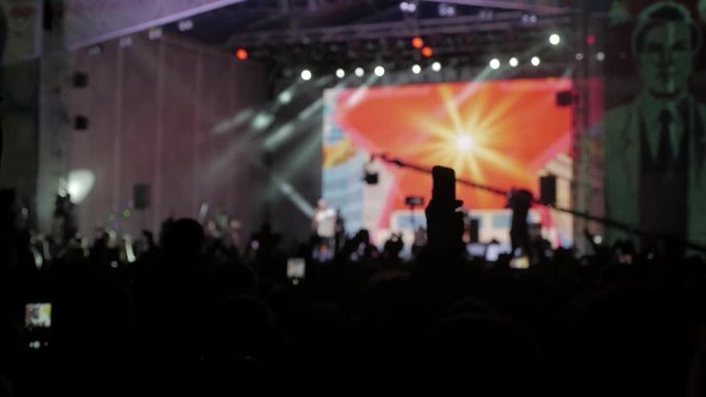 Crowd people at music concert . Cheering crowd takes pictures on a smartphone in front of bright colorful stage lights . silhouettes of concert crowd in front stage lights of bright . crowd of