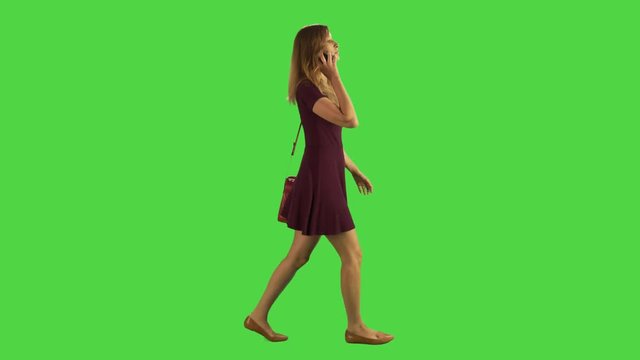 A young woman walking sideways and answers a phone call, talks and hangs in a full body shot over a green screen.