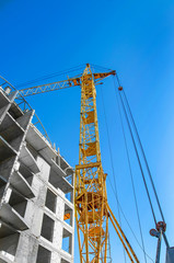 Yellow construction crane at a construction site near an unfinished building of concrete blocks on a background of blue sky. Construction technologies, expansion of cities, employment, job search