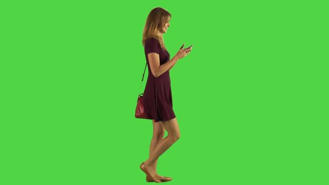 Young woman walking while texting. Happy.  Full body shot over green screen. Two takes.