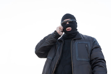 a man, a terrorist, a bandit in a black leather jacket and a mask talking on the phone