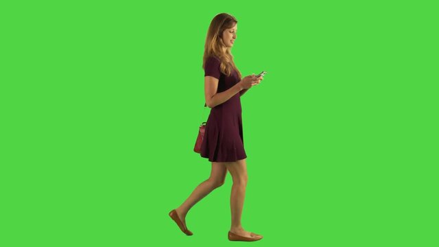 A young woman walking sideways and chatting in an app, full body shot over a green screen.