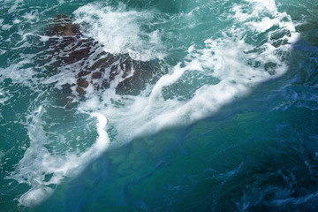 Azure waves at the rocks, in the sun and in the shade, background