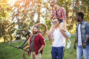 Young BMX rider in company with his multiethnic friends walking to have a good time at the city...