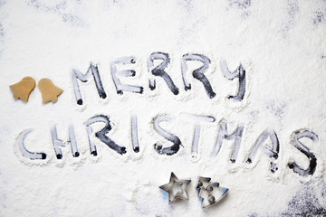 Christmas cooking: inscription merry christmas made from flour on a dark table, ingredients for baking and dried fruits on dark background