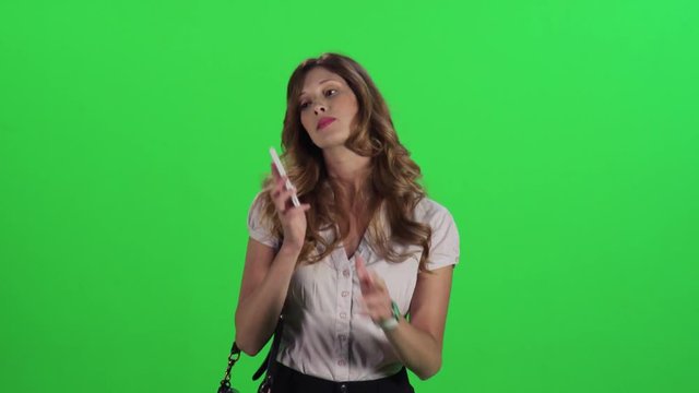 A young businesswoman walking in a medium frontal shot over a green screen, answers a call, talk and laugh, hangs.