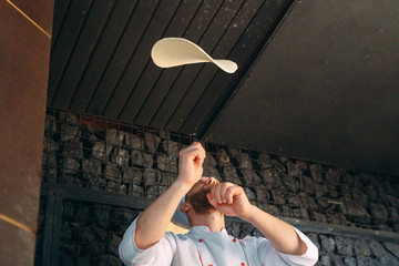 Skilled chef preparing dough for pizza rolling with hands and throwing up.