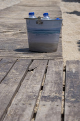 Naklejka premium Metallic bucket filled with bottled water on a wooden substrate in a beach