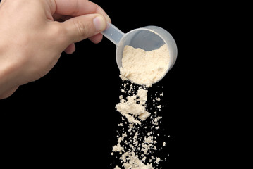 Pot of Whey Protein. Pouring whey protein into the pot with the scoop. Pouring white powder into the recipient black background.