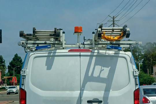The back end of a white utility van carrying ladders on its racks.