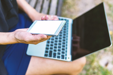 Woman holding mobile phone with blank white and laptop on outdoor. Lifestyle technology concept.