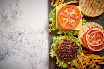 Two tasty grilled home made burgers with beef, tomato, onion and lettuce. French frides on side. Top view with copy space