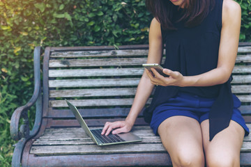 Close-up of hand woman working using mobile phone and laptop computer outdoor. Technology outdoor concept.