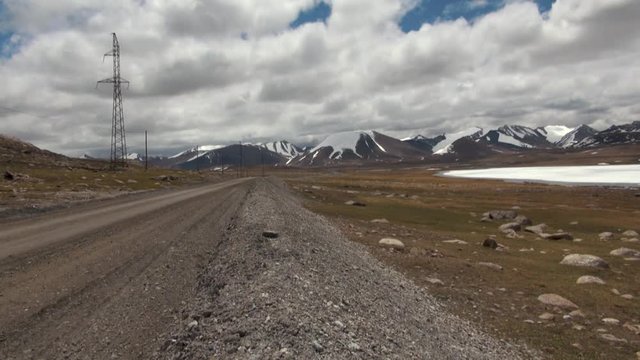 Mountain Road Through the Sujuk Pass in Kyrgyzstan With Dramatic Clouds, Rugged Peaks, and a Remote Dirt Path Winding Through High-Altitude Landscapes in Central Asia