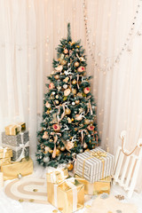 Luxury new year decor. Beige, light pink, golden, silver Christmas tree decoration. Merry Christmas and Happy Holidays! Bright lights and white interior.