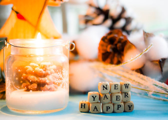 Christmas background - a burning candle in the form of Christmas trees, cones, toys and the inscription from white cubes with black letters 