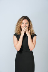 beautiful business woman in glasses in black dress on a gray background. happy face. she closed her mouth with her palms in surprise, looking at the camera.