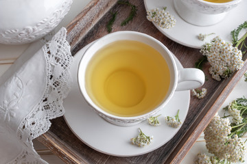 Obraz na płótnie Canvas Yarrow tea in a white cup with blooming yarrow twigs