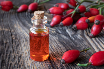 A bottle of rose hip seed oil with fresh rose hips on a wooden background